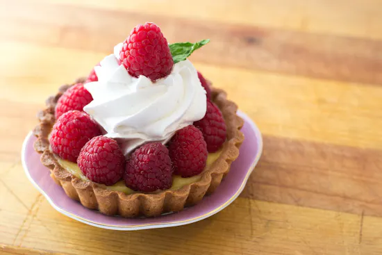Kleines Törtchen mit Himbeeren und Sahne auf Holzbrett